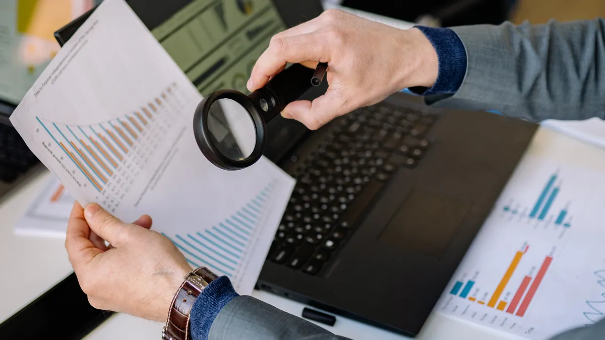 Bulk AI Content Quality Control — The Complete Guide hands checking charts and papers beside a laptop