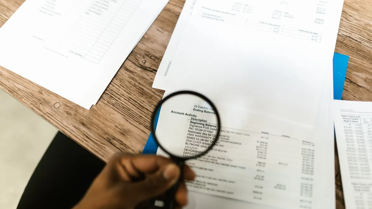 hand reviewing stacked documents with a magnifying glass