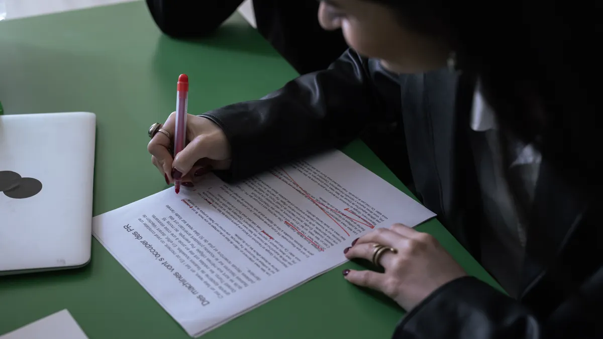 person proofreading a printed page with a red pen